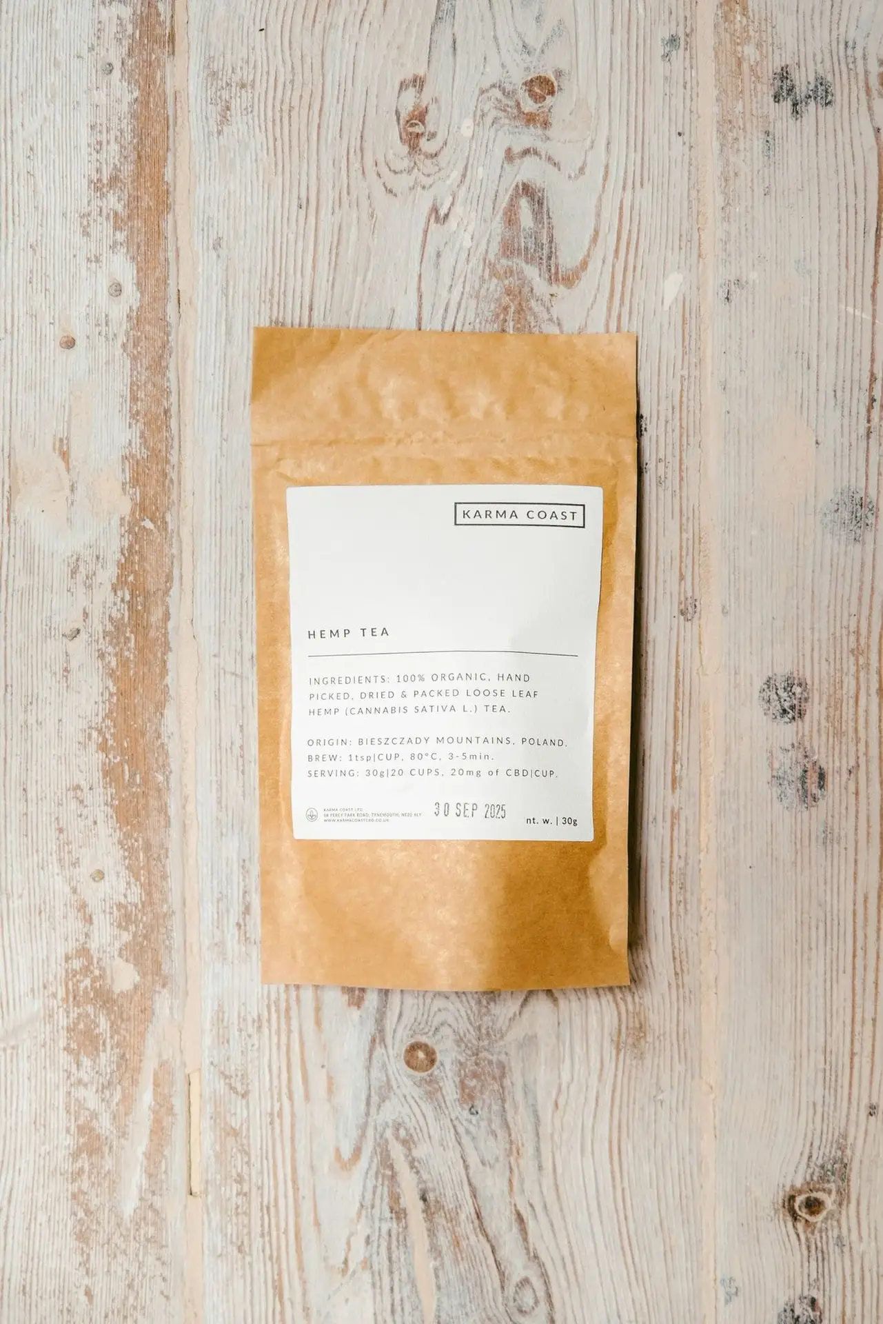 KARMA ORGANIC CBD TEA 1 A brown paper packet of KARMA ORGANIC CBD TEA rests on a light wooden surface. The white label displays the ingredients and expiry date. Ideal for those seeking CBD tea UK options, the sealed packet is centrally positioned.