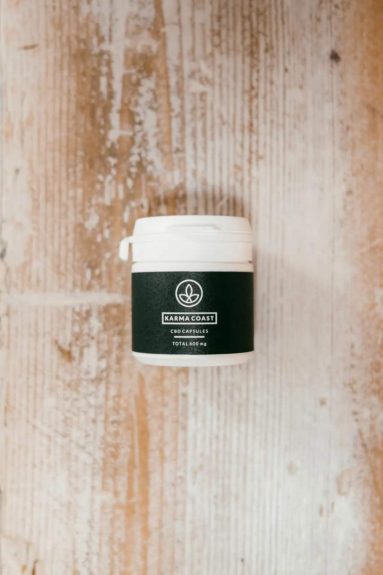 600mg CBD Capsules 1 A white container featuring a dark green label that reads "600mg CBD Capsules" rests on a light, rustic wooden surface.