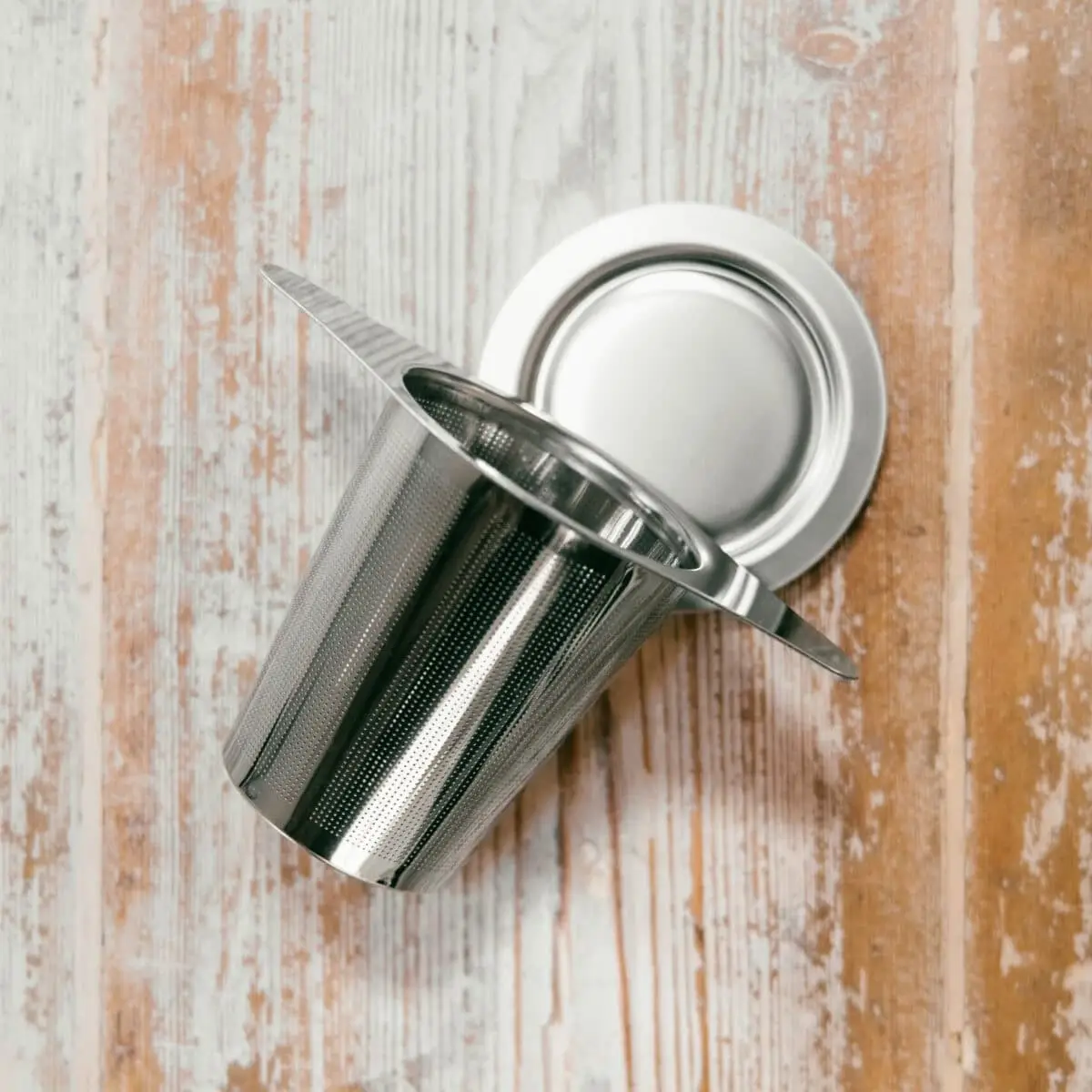 A KARMA TEA STRAINER with a lid is displayed on a rustic wooden surface with faded paint.