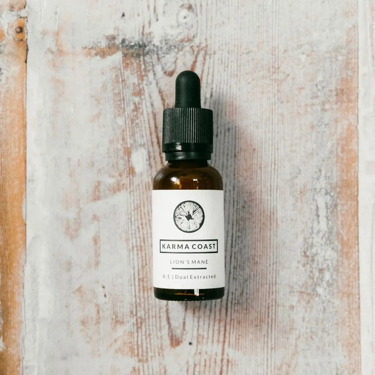 A small brown glass dropper bottle labelled Dual Extract Lion’s Mane Tincture sits on a distressed white wooden surface.