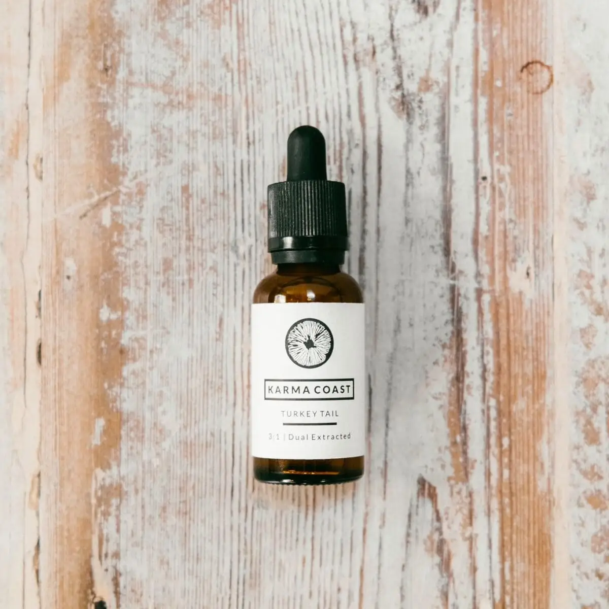 A brown glass dropper bottle labelled Turkey Tail Dual Extract Tincture sits on a rustic, whitewashed wooden surface.