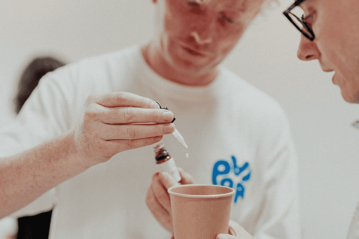 Finding Balance: The Benefits of Reducing Alcohol and How CBD Can Help 3 A person in a white shirt uses a pipette to add liquid into a brown paper cup whilst another person wearing glasses watches closely, perhaps discussing the benefits of reducing alcohol during their experiment.