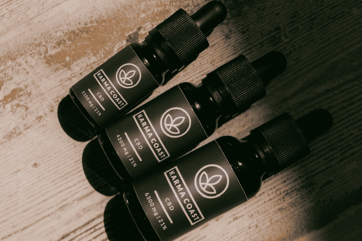 Finding Balance: The Benefits of Reducing Alcohol and How CBD Can Help 2 Three dark glass dropper bottles labelled Karma Coast CBD lay on a wooden surface, arranged diagonally. The bottles have black labels and caps, and light shines softly across the scene, subtly highlighting the benefits of reducing alcohol by choosing mindful alternatives like CBD.