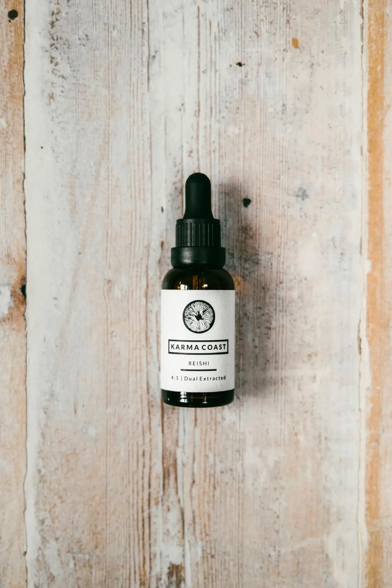 Reishi Dual Extract Tincture 1 A brown glass dropper bottle labelled Reishi Dual Extract Tincture rests on a light, rustic wooden surface. The label features a circular logo and text describing the product as dual extracted.