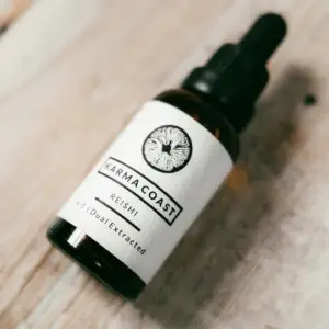 A small brown glass dropper bottle labelled Karma Coast Reishi 4:1 Dual Extracted lies on a light wooden surface.